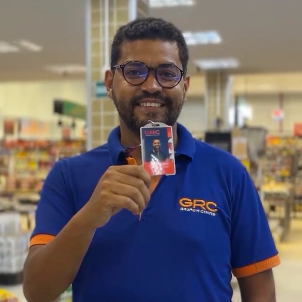 Colaborador do Grupo R Center sorrindo e mostrando o crachá dentro da loja