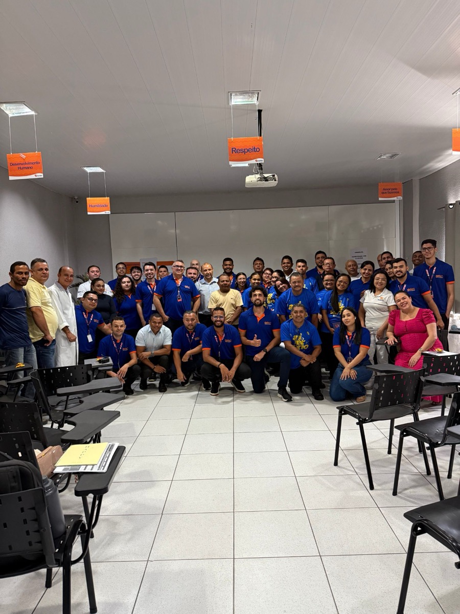 Equipe R Center reunida e sorrindo em uma sala de treinamento, sob placas com os valores Respeito, Humildade, Desenvolvimento Humano e Amor pelo que fazemos